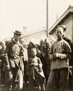 At a station on the Peking to Hankow railway line. A crowd of people gaze curiously into the camera