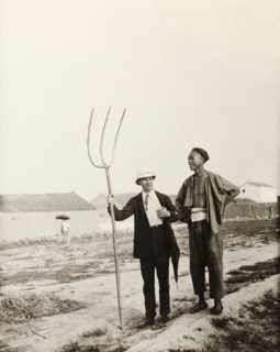 European man with Chinese farming tool. A European man, dressed in a suit and solatopi hat, holds a