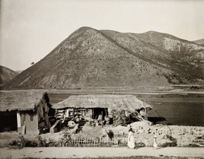Dwelling in the mountains, Korea. A small dwelling with a thatched roof sits at the edge of a flat
