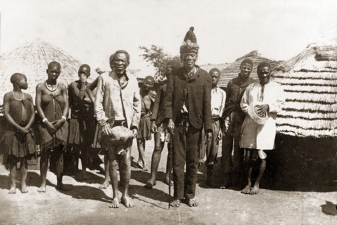 Chief Sekombo. Matabele (Ndebele) Chief Sekombo poses outside village huts with his witch doctor,