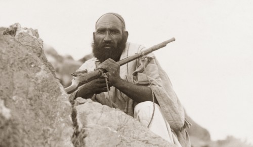 Portrait of an armed Afridi man. Portrait of an armed Afridi man, crouched behind a rock at Kohat