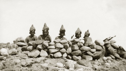 Five frontier guards. Five armed guards, dressed in uniforms and turbans, peer over the top of a