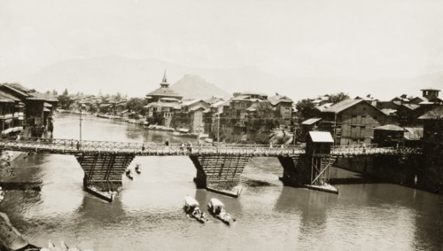 The Jhelum River at Srinagar. Several shikaras pass beneath a wooden road bridge spanning the
