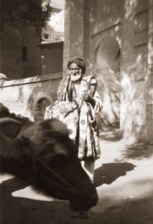 An Indian rug vendor. An elderly street trader touts a variety of patterned rugs as he wanders