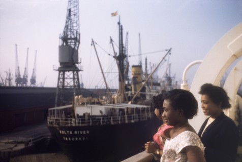 Shipping at Tilbury Docks. Three West African women gaze over the side of a ship moored at Tilbury