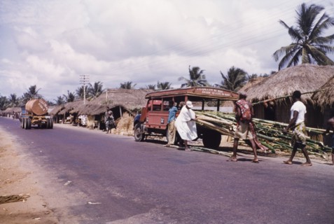 Unloading bamboo near Cape Coast'. Men unload bamboo from an open-sided truck at a roadside near