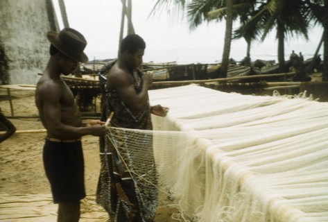 Mending the nets. Two men repair fishing nets at Anomabu beach. Anomabu, Ghana, January 1958.