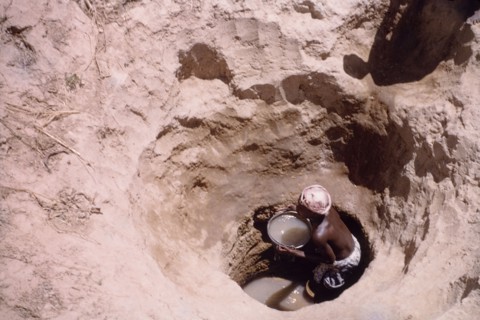 Waterhole near Tamale. A Ghanaian woman collects water in a pail from the bottom of a deeply-dug