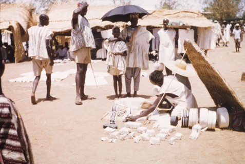 Woven cloth at Bawku market. A trader sells woven strip cloth from beneath a thatched sun shelter