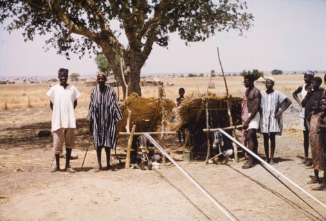 Boys weaving cloth at Pusiga, Ghana. Two young boys sit outdoors beneath thatched sun shelters as