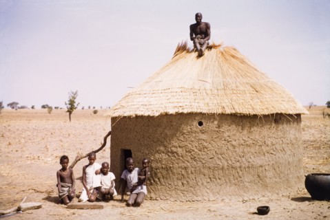 Roof thatcher in northern Ghana. A roof thatcher sits atop a round mud hut in Kuka. Thatchers in