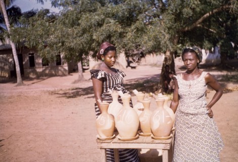 Water cooler sellers at Koloenu. Two female water cooler sellers stand at their roadside stall.
