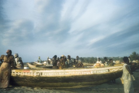Waiting on the beach at Saltpond. Several women wait beside painted fishing boats lying on a beach
