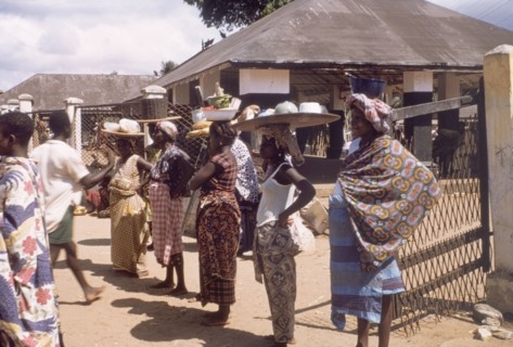 Traders watch an independence procession. Female market traders balance trays of food on their