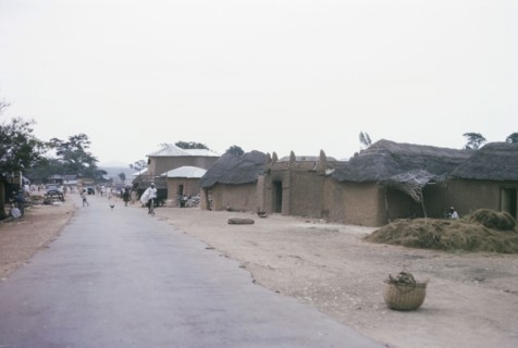 Main road through a Hausa village. Low, mud-walled buildings flank the main road running through a