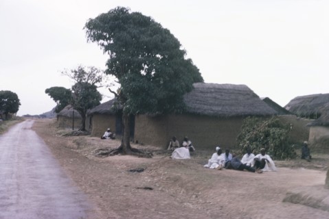 A Hausa village. Inhabitants of a Hausa village sit on the ground outside several square,