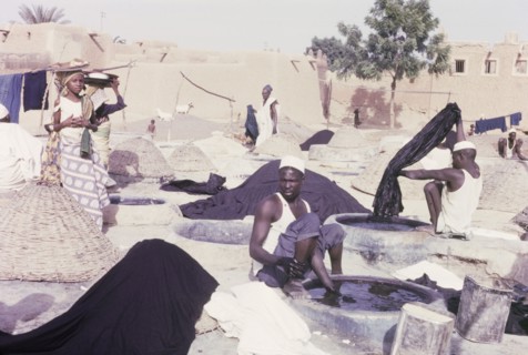 Indigo dyeing at Kano. Female hawkers circulate amongst textile workers who sit outdoors, dipping