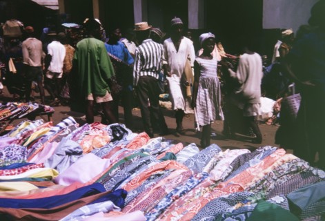 Cloth for sale in Freetown. Shoppers walk past a colourful market stall selling patterned rolls of