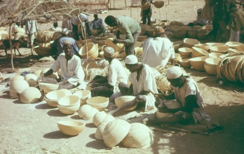 Hausa potters decorating bowls. A group of Hausa potters sit outdoors, using metal tools to
