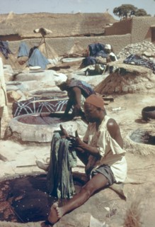 Hausa man dyeing fabric. A Hausa man sits beside a well of liquid dye, carefully dipping a section