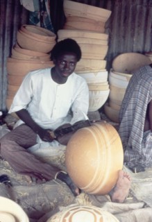 A Hausa potter decorates a bowl. A Hausa potter uses a metal tool to inscribe patterns onto a clay