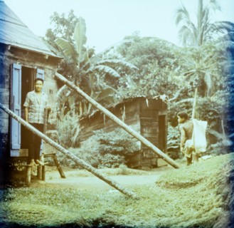 Rural housing in Dominica. A Dominican man stands in the doorway of a wooden house on stilts as a