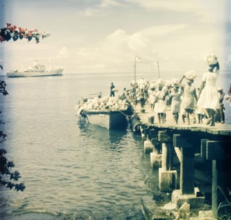 Maritime trade, Dominica. A group of women walk along a wooden pier carrying sacks on their heads,