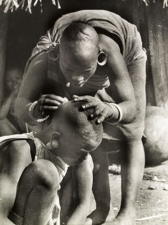 A Kikuyu mother de-louses her daughter. A Kikuyu mother bends over to de-louse her daughter's