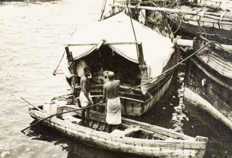 Attending to cargo at Old Mombasa harbour. Two men stand in a canoe, attending to cargo stored
