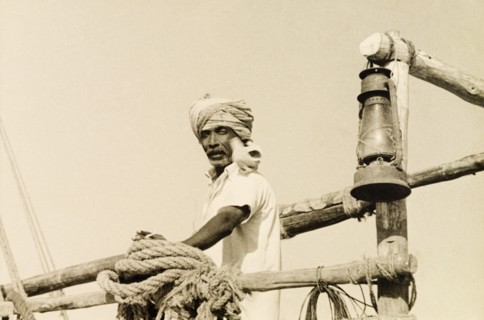 Sailor with a seabird. A turbaned dhow captain stands on the deck of his boat with a seabird