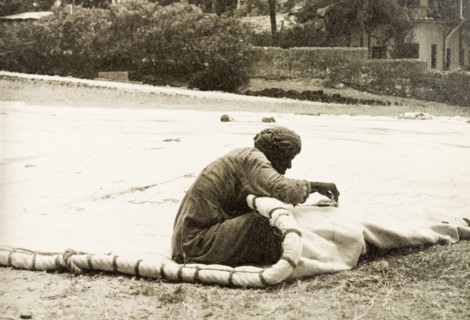 A sail maker repairs a dhow sail. A sail maker repairs a dhow sail on an open patch of ground below
