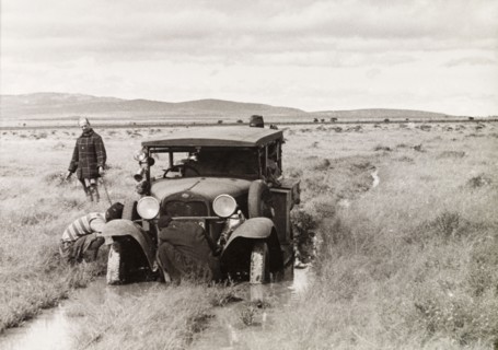 Stuck in the mud. Several men attend to a car, which is stuck in the mud on a flooded country track