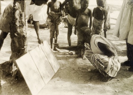 Adult literacy campaign, Gold Coast. A student teacher helps a man to read from a board propped up