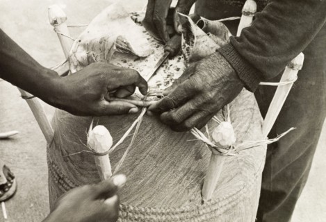 Securing the head of an atumpan drum. Two craftsmen secure the head of an atumpan drum by fastening
