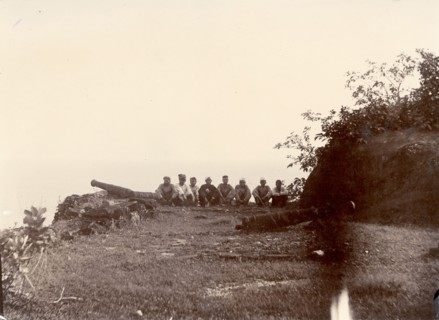 A bastion on Anjidiv Island. A row of men sit beside two cannons on the eastern bastion of a
