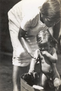 A European woman washes her child. A European woman bends over to wash her young child in a washtub