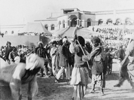 A display of swordsmanship. Musicians play as two swordsmen spar at an outdoor event. Sukkur, Sind,