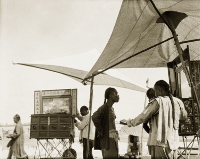 Peep boxes at a Chinese fair. Stallholders set up peep boxes beneath parasols at an outdoor fair.