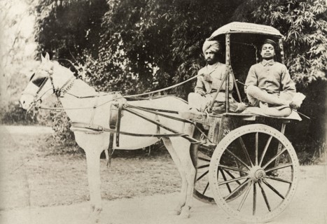 A horse-drawn tonga. An Indian driver and his passenger sit cross-legged on a horse-drawn tonga.