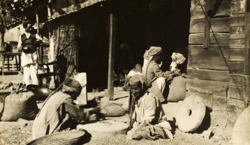 Indian millers at work. A group of men sit outdoors as they grind grain by hand using millstones.