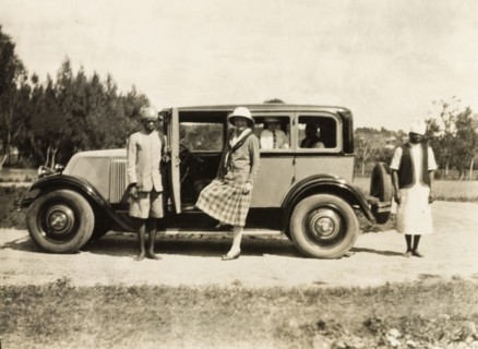 A head servant holds open a car door. An African head servant holds open the door of a car as a