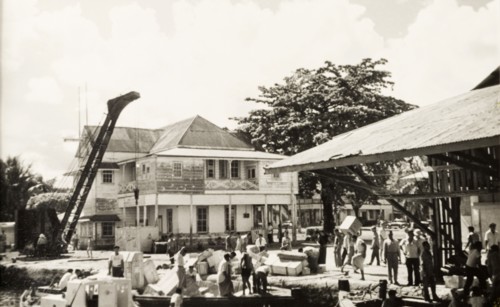 Unloading goods at Apia wharf. Crates of goods are unloaded from barges at a wharf in the port city