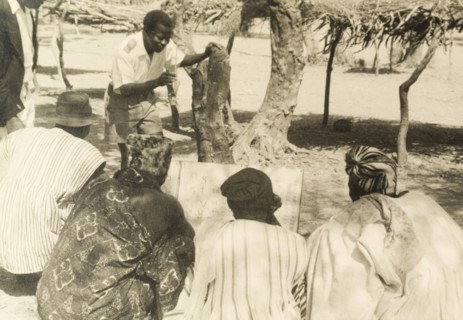 Adult literacy campaign, Gold Coast. A student teacher helps men to read from a board during a