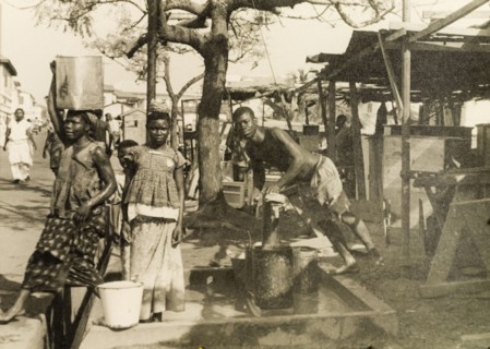 Collecting water from a hand pump, Accra. Men and women collect water from a hand pump on a street