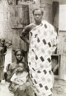 An Asante family. An Asante (Ashanti) man stands beside his seated wife and baby, wearing a