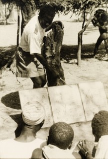 Adult literacy campaign, Gold Coast. A student teacher helps men to read from a board during a