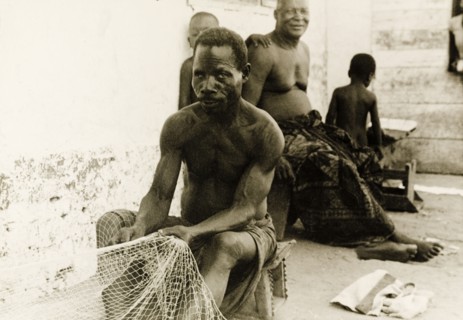 Fisherman repairing his nets, Ghana. A fisherman sits on a stool at the side of a street as he