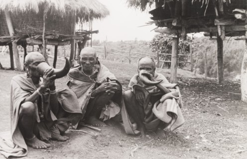 Kikuyu elders drinking beer. Three Kikuyu elders squat on the ground as they drink beer from hollow