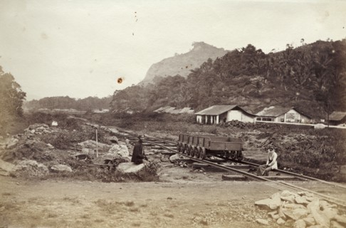A Ceylon Government Railway track. Two men sit beside an empty rail cart on tracks belonging to the