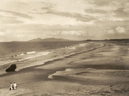 Malabar Coast and Mount Deli. Two tiny figures walk along a vast sandy beach on the Malabar Coast